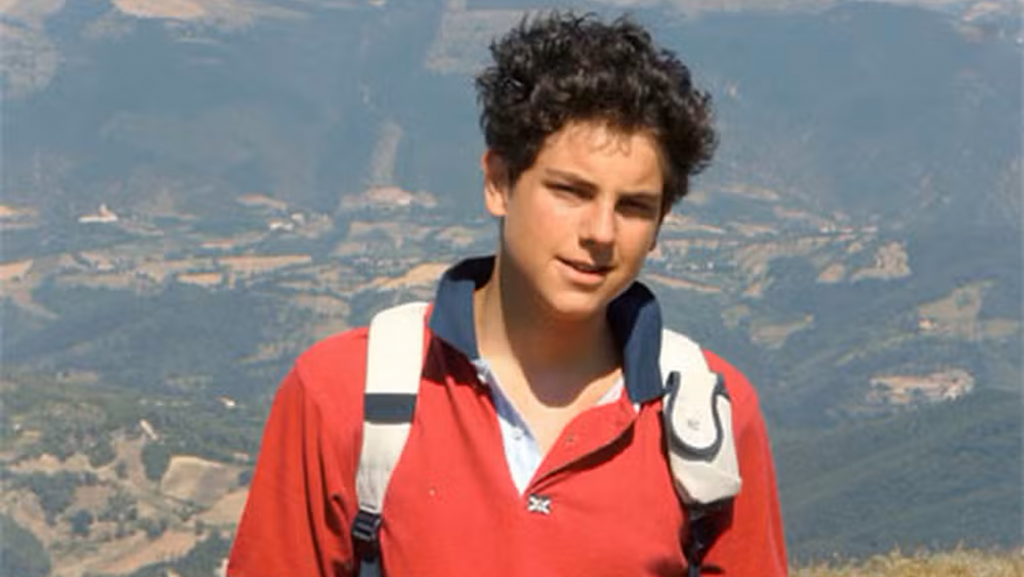 Carlo Acutis durante trilha em pico de morro com cidade ao fundo