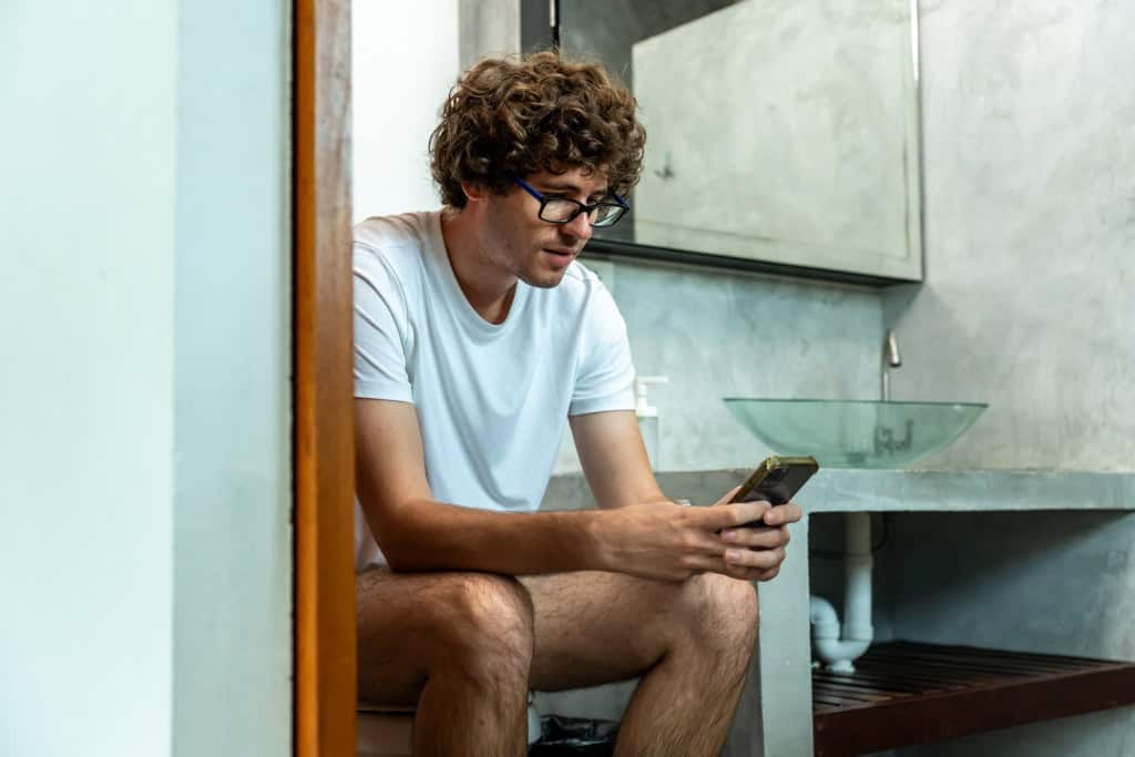 Homem sentado na privada (vaso sanitário) com o celular na mão