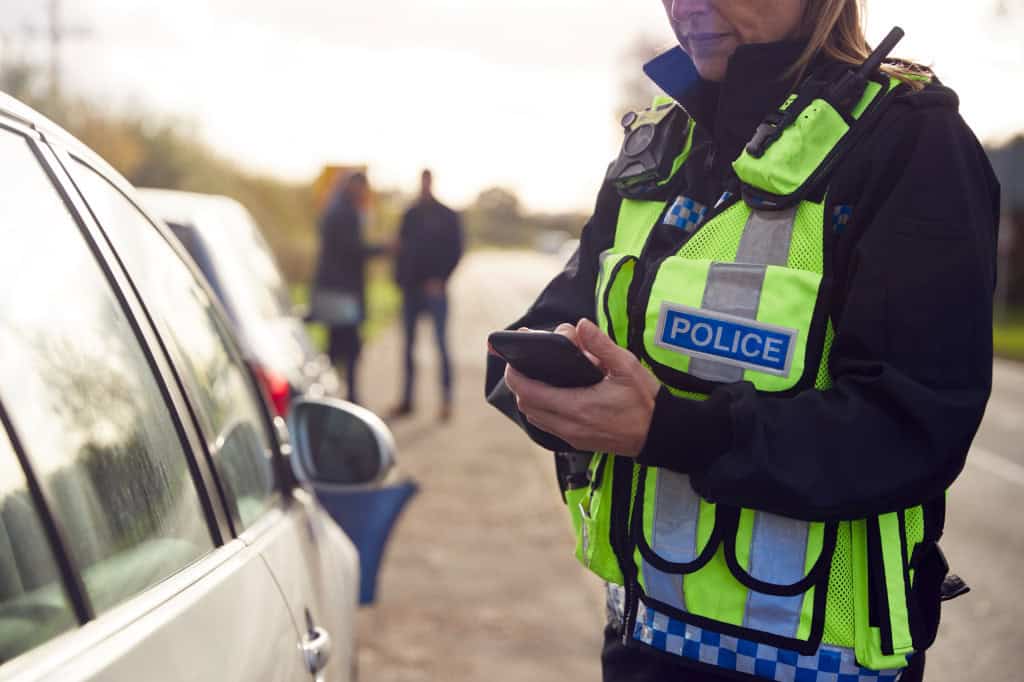 Policial com um celular na mão ao lado de um carro