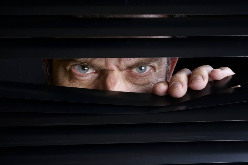 Homem espionando através de veneziana