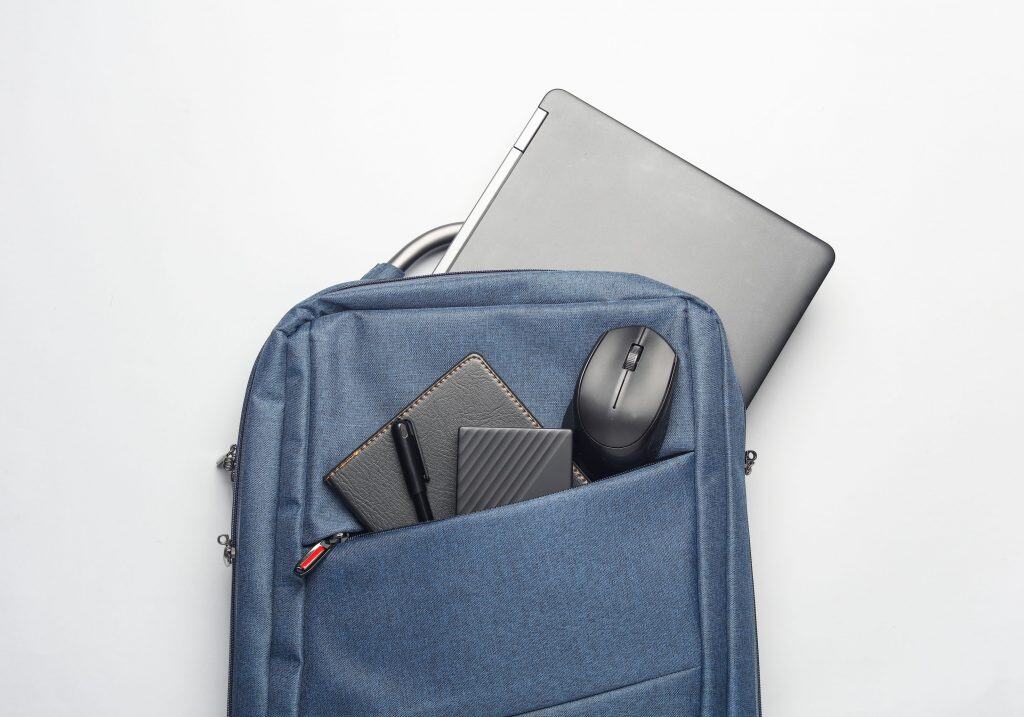 Gadgets modernos para trabalho e estudo. Mochila com notebook, disco rígido externo e mouse em fundo branco.