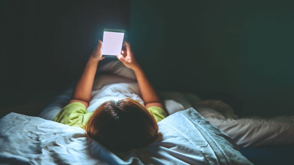 Mulher asiática jogando no smartphone na cama à noite.