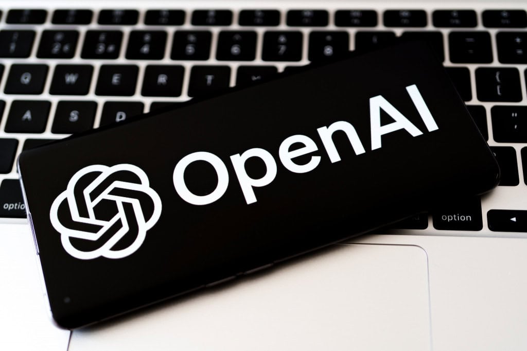 Logo da OpenAI em um smartphone que está em cima do teclado de um notebook